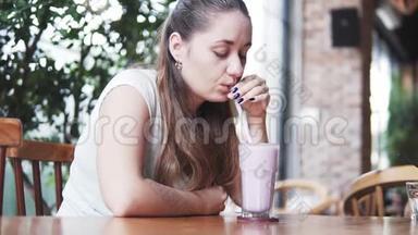 年轻漂亮的欧洲女孩在炎热的夏日在咖啡馆里喝着冰镇牛奶鸡尾酒和蓝莓。 妇女饮酒
